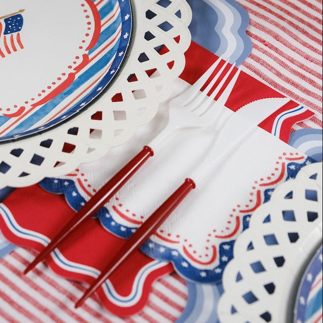Red, white, and blue tableware with decorative doilies on a matching tablecloth.